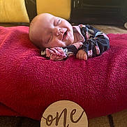 Delilah joined the competition — help win amazing prizes! baby, infant, smiling, sleeping, one_month, cushion, blanket, wooden_sign, floral_clothing, indoor, carpet, cute, resting, young_child, portrait, newborn, soft_texture, happy, peaceful, milestone