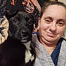 woman, dog, puppy, black_dog, white_patch, smiling, selfie, robe, indoor, tapestry, colorful_background, portrait, cozy, pet, companion, face, cute, furry, happy, casual