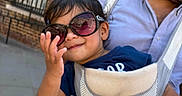 Soham joined the competition — help win amazing prizes! adult, baby_carrier, blue_shirt, brick_building, carrier, child, daylight, family, fashion, outdoor, parent, pink_clothing, portrait, smiling, street, sunglasses, toddler, travel, urban, window