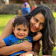 Soham is registered to the contest to win money with this photo: adult, blue_shirt, child, family, family_photo, flowers, garden, grass, happy, hugging, long_hair, mother, outdoor, portrait, ring, sitting, smiling, sunlight, toddler, watch
