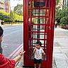 Soham joined the competition — help win amazing prizes! architecture, buildings, casual_clothing, child, city, daylight, london, outdoor, portrait, red, road, sidewalk, smiling, standing, street, telephone_box, toddler, tourism, travel, trees
