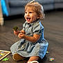 toddler, child, smiling, blue_dress, broccoli, puzzle_pieces, wooden_floor, sitting, happy, indoor, curly_hair, shoe, toy, play, person, couch, blurred_background, cute, young_child, casual_clothing