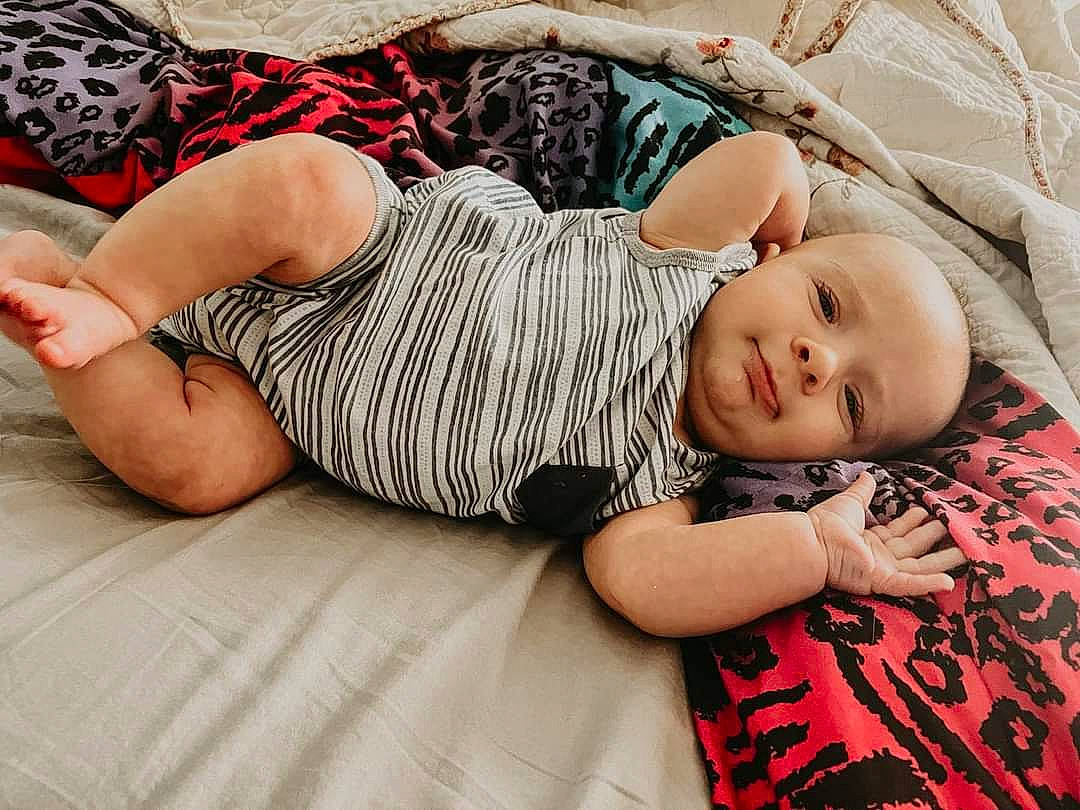 Alden is registered to the contest to win money with this photo: baby, baby_toddler_clothing, child, comfort, couch, foot, grass, human_leg, knee, leg, linens, pattern, person, sitting, skin, sleeve, sunglasses, t_shirt, thigh, toddler