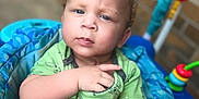 Kobe joined the competition — help win amazing prizes! baby, child, blue_eyes, green_shirt, cartoon_print, baby_seat, toy, orange, indoor, brick_wall, curly_hair, expression, pointing, closeup, infant, colorful, playful, portrait, seat, person