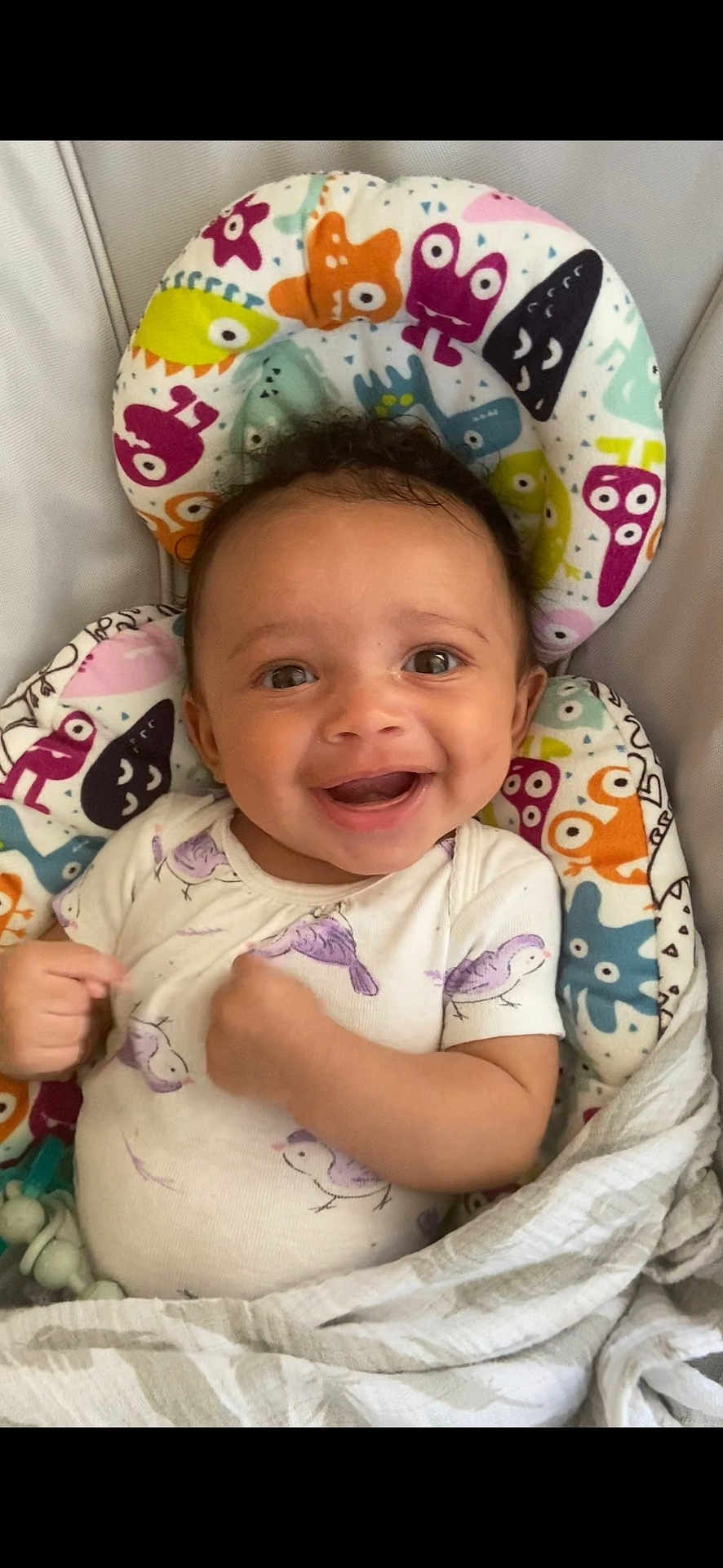 Octavia is registered to the contest to win money with this photo: baby, smiling, infant, cute, onesie, bird_print, blanket, cushion, colorful, patterned, happy, face, child, portrait, indoors, soft_toys, comfort, expression, young, cozy