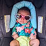 baby, child, car_seat, sunglasses, colorful_clothing, floral_pattern, infant, seat_belt, head_support, cute, small_hands, legs, bright_colors, accessory, fashion, toddler, babywear, comfort, relaxed, indoor