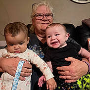 Emmett joined the competition — help win amazing prizes! babies, grandmother, family, infants, smiling, portrait, indoors, couch, sitting, holding, caregiver, glasses, blonde_hair, black_clothing, floral_clothing, baby_bottle_absent, living_room, wall_clock, happy, family_photo