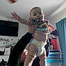 Emmett is registered to the contest to win money with this photo: baby, infant, child, adult, holding, standing, diaper, shirt, smiling, portrait, indoor, living_room, television, furniture, curtain, ceiling_fan, home, family, playful, photography