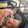 baby, infant, stroller, portrait, face, eyes, smiling, curious, reaching, lying_down, clothing, striped_clothing, stuffed_animal, toy, yellow_toy, blanket, canopy, outdoor, close_up, child