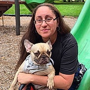 Gwennifer joined the competition — help win amazing prizes! woman, dog, french_bulldog, glasses, playground, slide, harness, leash, outdoor, grass, trees, wood_chips, casual_clothing, smile, pet, holding, sitting, person, animal, park