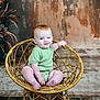 Ava is registered to the contest to win money with this photo: baby, child, red_hair, blue_eyes, green_onesie, woven_chair, sitting, smiling, indoor, rustic_background, floral_arrangement, floor, cute, portrait, plush, person, furniture, cozy, warm_lighting, infant