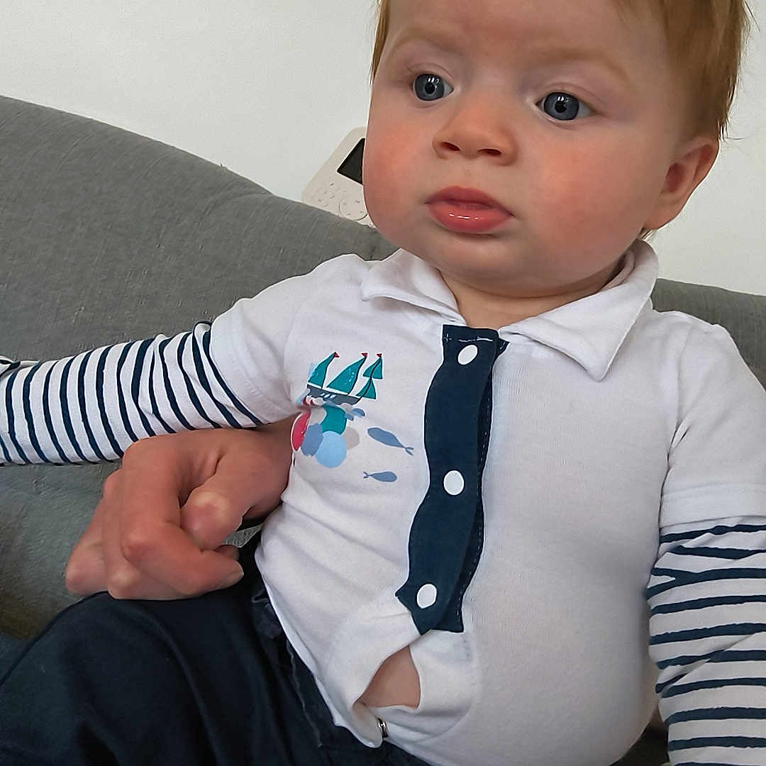 Leeroy participe au concours pour gagner de l'argent avec cette photo : baby, blue_eyes, casual_clothing, child, closeup, comfortable, couch, curious_expression, hand, home, indoor, infant, person, portrait, red_hair, seated, soft_lighting, striped_sleeves, supporting_hand, white_shirt