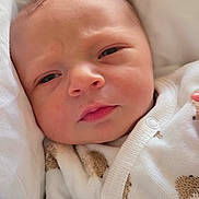 Noé a rejoint le concours — aidez-le/la à gagner de superbes lots ! baby, newborn, infant, face, closeup, white_clothing, patterned_clothing, bed, blanket, plush_toy, soft, cute, sleepy, hand, skin, indoors, portrait, young_child, cozy, resting