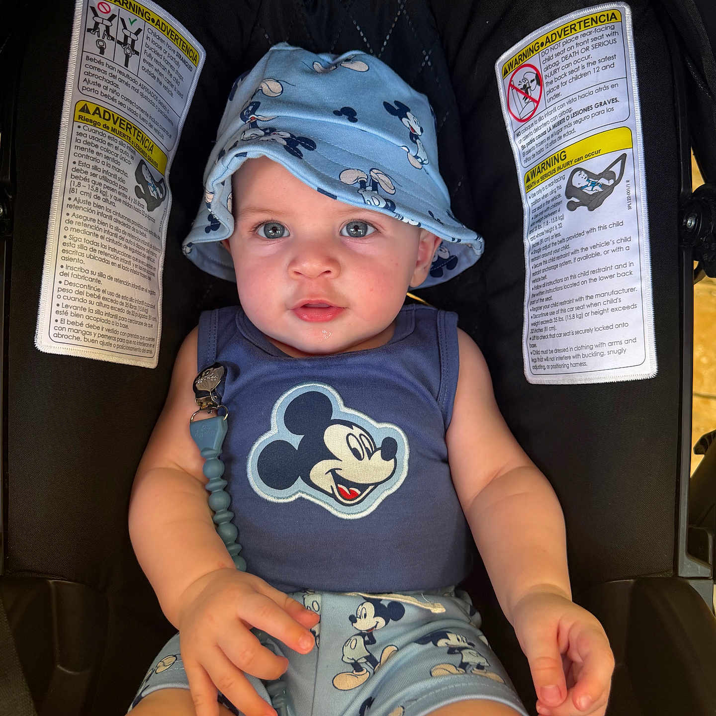 Levi joined the competition — help win amazing prizes! baby, child, mickey_mouse, hat, bucket_hat, blue_clothing, car_seat, seatbelt, infant, cute, face, person, sitting, smiling, warning_label, safety, indoor, closeup, hand, portrait