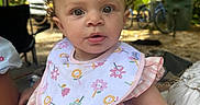 Willow joined the competition — help win amazing prizes! baby, child, infant, pink_bib, pink_dress, bow, curly_hair, outdoor, greenery, bicycle, person, face, cute, young_child, summer, daylight, portrait, sitting, attention, expression