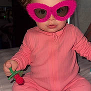 Willow is registered to the contest to win money with this photo: baby, pink_onesie, curly_hair, pacifier, toy, glasses, indoor, bed, cute, child, novelty_glasses, sitting, infant, face, person, playful, cozy, soft_lighting, expression, young_child