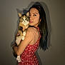 woman, cat, calico_cat, red_dress, tattoo, portrait, indoor, shadow, long_hair, holding, looking_at_camera, pet, animal, human, face, expression, cute, calm, warm_lighting, close_up