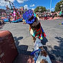 dog, costumed_character, parade, float, crowd, outdoor, daytime, sky, clouds, street, leash, people, flag, tree, shadow, colorful, amusement_park, fun, interaction, celebration