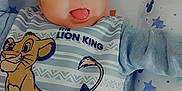 Maël participe au concours pour gagner de l'argent avec cette photo : baby, infant, smiling, tongue_out, lion_king, simba, onesie, blue_clothing, lying_down, cushion, stars_pattern, mickey_mouse_pattern, cute, happy, child, face, portrait, indoor, playful, young_child