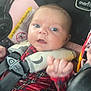 baby, infant, child, car_seat, harness, seatbelt, buckle, closeup, portrait, surprised, blue_eyes, plaid_clothing, red_clothing, head, face, hand, safety_label, padding, travel, cozy