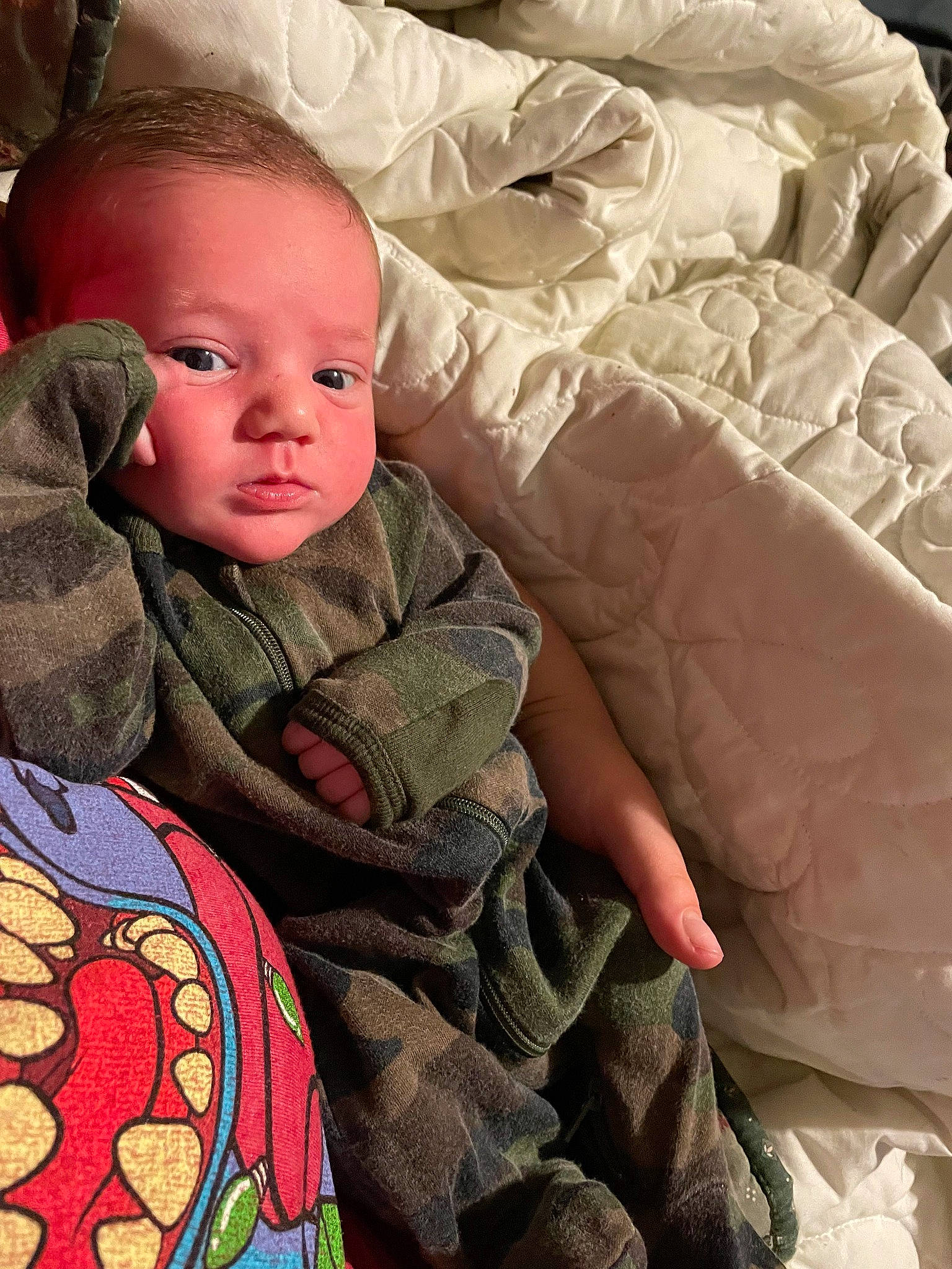 Chase is registered to the contest to win money with this photo: baby, baby_toddler_clothing, bedding, cheek, child, comfort, facial_expression, finger, head, linens, mammal, mouth, nose, outerwear, person, sitting, skin, sleeve, textile, toddler