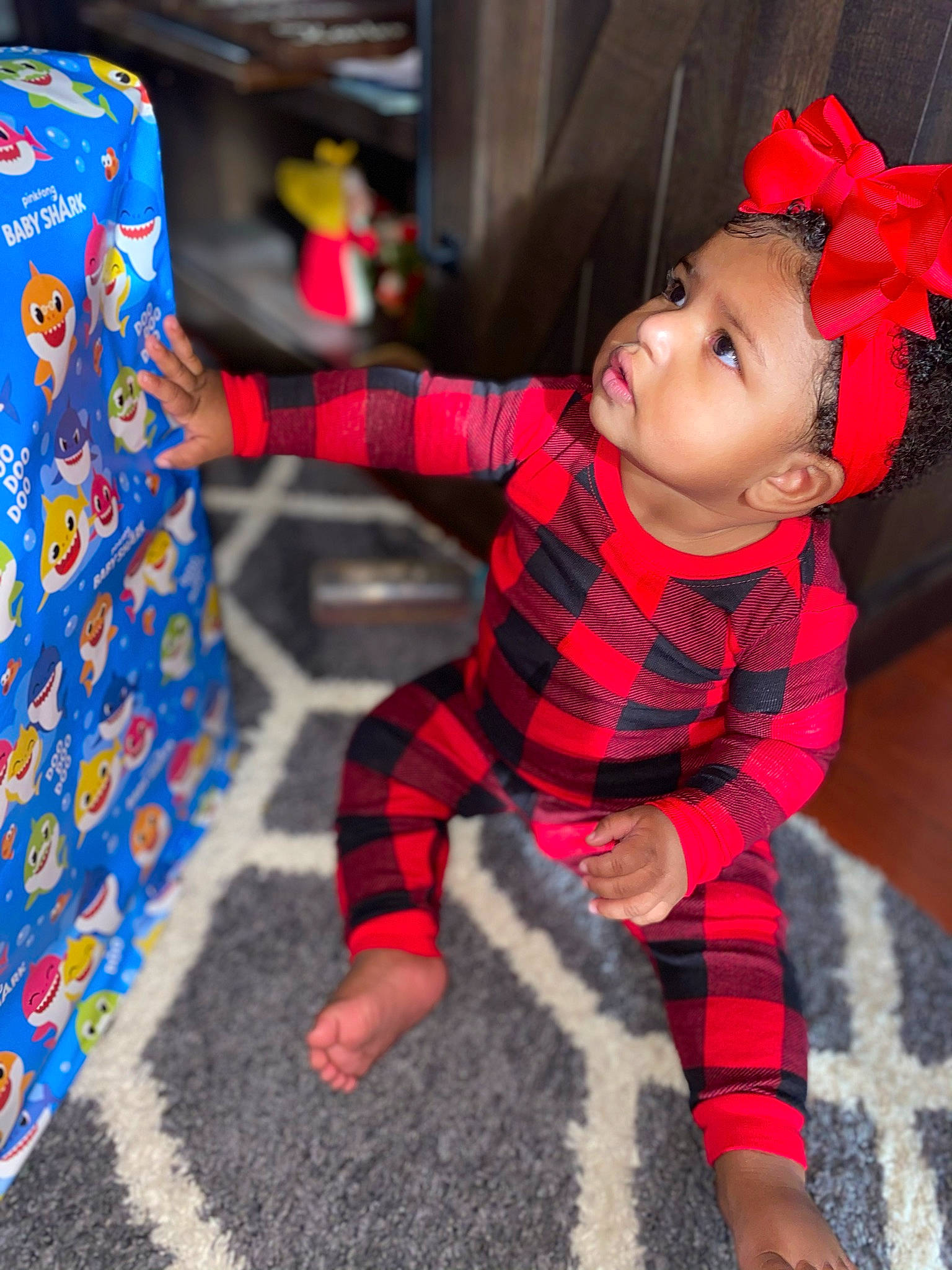 Janiylah joined the competition — help win amazing prizes! baby, christmas, doll, face, flooring, headwear, human_body, human_leg, leg, pattern, person, plaid, plant, red, sleeve, sock, stuffed_toy, tartan, textile, thigh