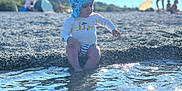 Amir a rejoint le concours — aidez-le/la à gagner de superbes lots ! background, beach, blue, casual_clothing, child, daylight, nature, outdoor, pebbles, people, playing, reflection, scenery, sitting, summer, sunhat, sunlight, toddler, vacation, water