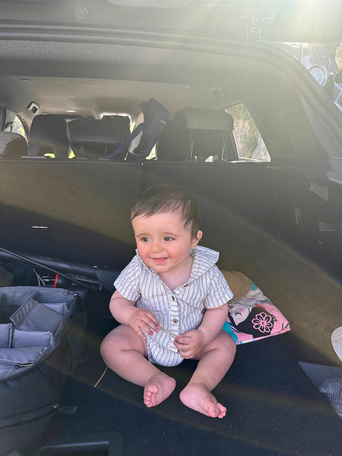 Amir participe au concours pour gagner de l'argent avec cette photo : baby, child, car_trunk, onesie, sitting, smiling, sunlight, lens_flare, travel_gear, towel, hat, foot, hand, hair, head, face, happy, indoor, vehicle, seat