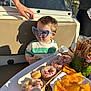 bench, boat, casual_clothing, child, chips, donuts, food, hand, heart_shaped, outdoor, person, plastic_cup, pretzels, reflection, shadow, snack, summer, sunglasses, sunlight, table