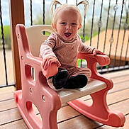 Pais is registered to the contest to win money with this photo: toddler, child, smiling, pink, rocking_chair, plastic_chair, pigtails, blonde_hair, outdoor, balcony, wooden_deck, portrait, happy, black_boots, seat, playtime, person, face, depth_of_field, cute
