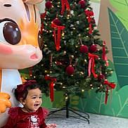 Rhema is registered to the contest to win money with this photo: toddler, child, dress, red, bow, smiling, christmas_tree, decorations, lights, toy, cartoon, indoor, floor, holiday, festive, happy, cute, person, celebration, background