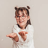 Judith participe au concours pour gagner de l'argent avec cette photo : child, girl, glasses, smiling, happy, bubbles, white_shirt, casual, jeans, portrait, indoor, cute, hair_buns, playful, hands_out, joyful, fashion, young, studio, light_background