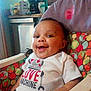 Dallas is registered to the contest to win money with this photo: baby, high_chair, smiling, tshirt, love_machine, indoor, kitchen, appliances, colorful, pattern, face, child, person, happy, seatbelt, table, food_preparation, domestic, cute, infant