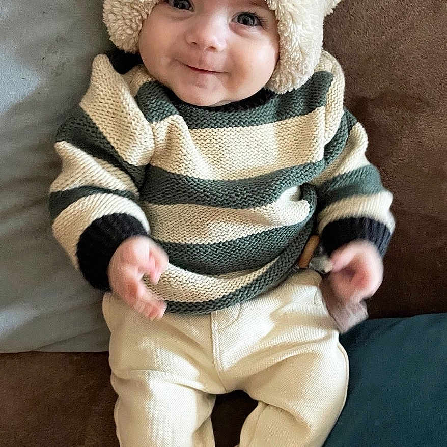 Mylan a rejoint le concours — aidez-le/la à gagner de superbes lots ! baby, bear_hat, child, clothing, couch, cozy, cushion, cute, happy, hat, indoor, infant, pants, person, portrait, seated, smile, socks, striped_sweater, young_child