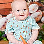baby, child, blue_eyes, carrot_pattern, toy, sitting, smiling, cute, infant, outfit, wooden_background, flowers, decor, portrait, happy, indoor, plush, small_hands, feet, bright