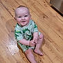 Garrett is registered to the contest to win money with this photo: baby, child, smiling, sitting, floor, wooden_floor, dinosaur_pattern, clothing, indoors, person, cute, playful, young_child, infant, happy, skin, feet, hands, head, face