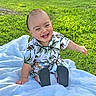 baby, child, smiling, laughing, outdoor, grass, blanket, shirt, tropical_print, footwear, happy, cute, sitting, sunlight, greenery, nature, portrait, infant, casual_clothing, daytime