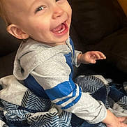 James is registered to the contest to win money with this photo: toddler, child, smiling, happy, blanket, hoodie, blue_stripes, indoor, couch, seated, face, person, cozy, cute, young_child, laughing, clothing, home, portrait, warm_lighting