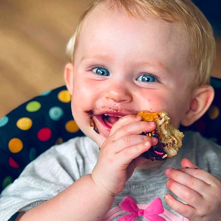 Oakland joined the competition — help win amazing prizes! baby, child, infant, smiling, happy, blue_eyes, blond_hair, portrait, close_up, eating, food, messy_face, hands, sitting, high_chair, polka_dots, indoor, colorful, bow, shirt