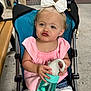 toddler, child, stroller, bow, water_bottle, pink_top, denim_shorts, lace_trim, pouting_face, outdoor, bench, concrete, cute, baby, person, summer_clothing, expression, sitting, holding, playful