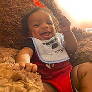 Cameron is registered to the contest to win money with this photo: baby, smiling, bib, blanket, cozy, happy, infant, child, face, portrait, cute, clothing, lying_down, indoor, warm_light, fuzzy, human, newborn, expression, soft