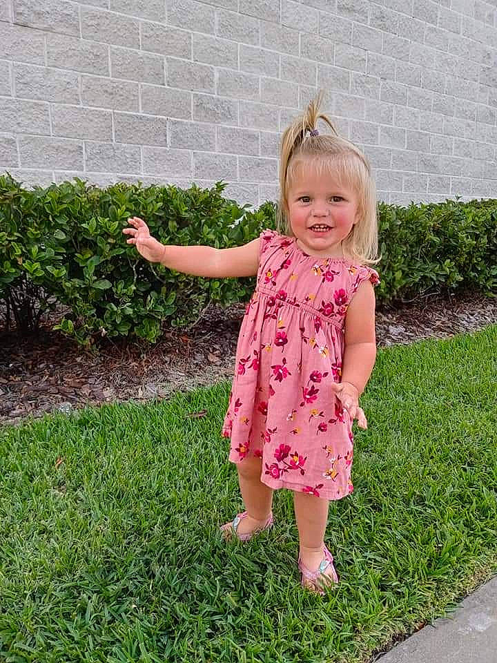 Haylee is registered to the contest to win money with this photo: baby_toddler_clothing, botany, child, clothing, day_dress, dress, fun, grass, groundcover, hand, happy, joy, lawn, magenta, one_piece_garment, people_in_nature, person, pink, plant, sleeve