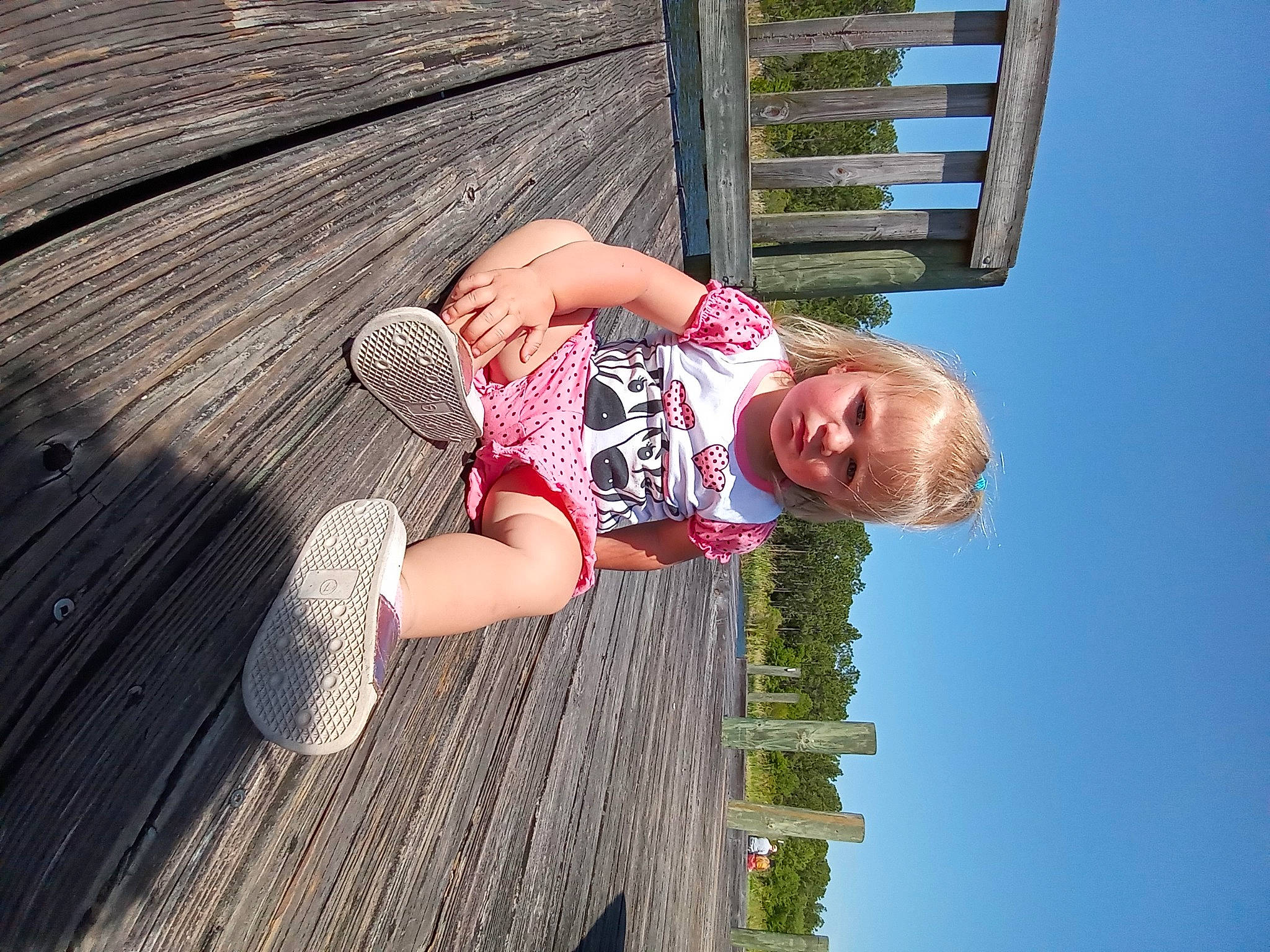 Haylee is registered to the contest to win money with this photo: child, deck, fun, grass, green, happy, hardwood, human_leg, leisure, people_in_nature, person, plank, sky, smile, thigh, toddler, tree, vacation, water, wood