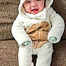 baby, smiling, onesie, costume, bear_theme, hood, couch, furniture, infant, cute, child, happy, plush, seated, indoor, cozy, clothing, portrait, young, person