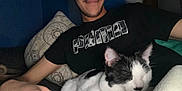 Jade joined the competition — help win amazing prizes! person, male, face, smile, mustache, black_and_white_cat, pet, indoor, pillow, blanket, t_shirt, logo, sofa, resting, feline, sleeping, close_up, cozy, flash, hand