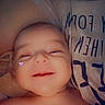 Paisley is registered to the contest to win money with this photo: baby, infant, smiling, sleepy, portrait, close_up, face, eyes, nose, mouth, bare_shoulders, adult, shirt, text_on_clothing, heart_sticker, cozy, indoor, candid, photograph, warm_lighting