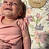 baby, infant, two_months, child, face, portrait, lying_down, pink_outfit, romper, floral_blanket, wooden_sign, milestone_photo, indoors, bed, baby_hand, blue_eyes, looking_at_camera, cute, newborn, photography
