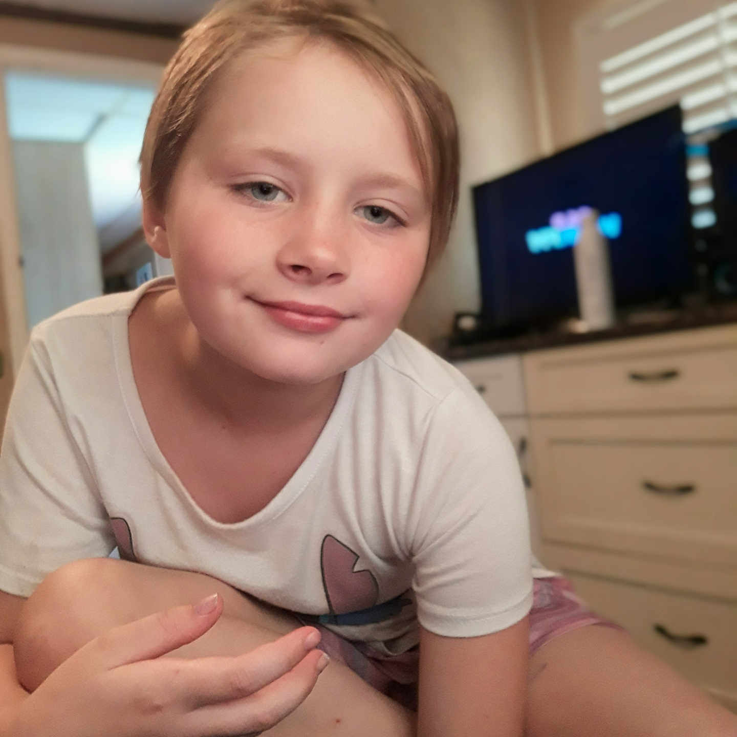 Josie joined the competition — help win amazing prizes! cabinet, casual_clothing, child, couch, face, furniture, hand, home, indoor, person, portrait, relaxed, short_hair, sitting, skin, smiling, television, white_tshirt, window_blinds, young
