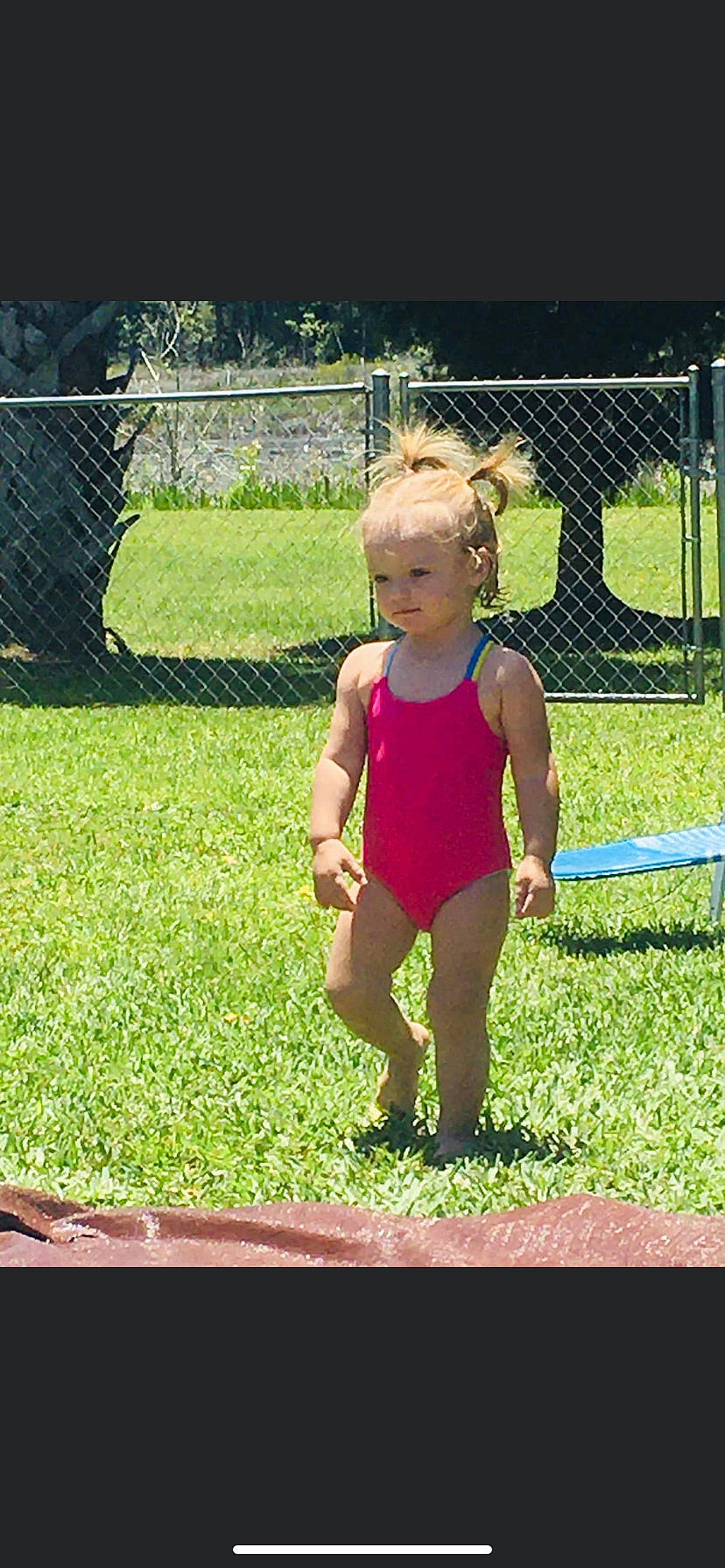 Bridget is registered to the contest to win money with this photo: baby_toddler_clothing, child, fence, fun, garden, grass, happy, headwear, human_leg, lawn, leisure, mesh, one_piece_swimsuit, people_in_nature, person, plant, recreation, sportswear, swimwear, thigh