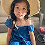 Mira is registered to the contest to win money with this photo: child, girl, hat, straw_hat, blue_dress, indoor, couch, portrait, young, sitting, long_hair, earrings, expression, face, person, home, furniture, natural_light, casual_clothing, soft_focus